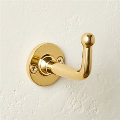 a close up of a gold robe hook on a white wall with no one in it