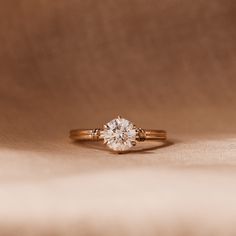 a diamond ring sitting on top of a white cloth covered surface with a light brown background