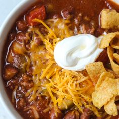 a white bowl filled with chili, beans and tortilla chips topped with sour cream