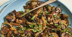 a blue plate topped with mushrooms and parsley next to a wooden spoon on top of a table