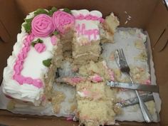 a half eaten birthday cake with pink frosting and flowers on it in a cardboard box