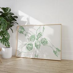 a green plant sitting in front of a white wall next to a framed art piece