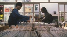 two people sitting at a table with stacks of records