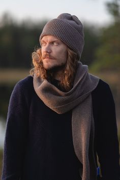 a man with long hair wearing a gray hat and scarf standing in front of a body of water