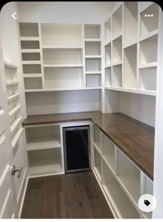 an empty room with white shelving and wood flooring in the center is a wine cellar built into the wall