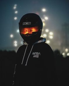 a person wearing a black jacket and helmet with lights in the back ground behind them