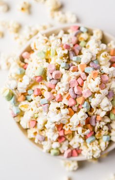 a bowl full of popcorn with marshmallows and sprinkles on the side