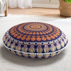 a blue and orange round pillow sitting on top of a white rug next to a potted plant