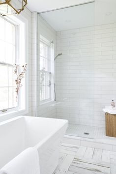 a white bathroom with a tub, sink and window