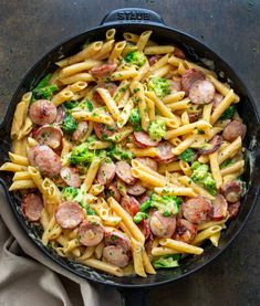 a skillet filled with pasta, sausage and broccoli on top of a table