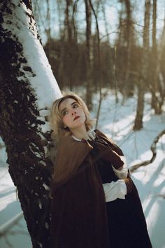 a woman standing next to a tree in the snow