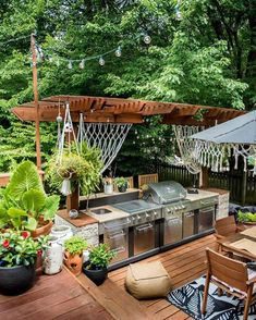 an outdoor kitchen and grill area with lots of greenery on the deck, surrounded by trees