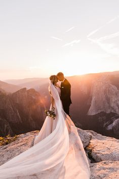 a bride and groom standing on top of a mountain at sunset with the sun behind them