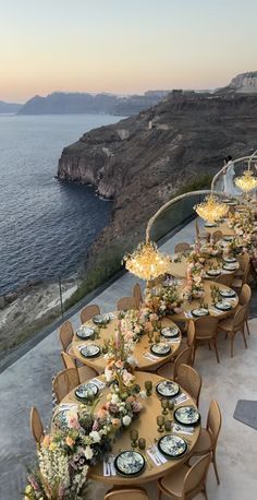 an outdoor dining area overlooking the ocean with flowers and plates laid out on it's tables