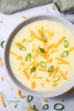 a bowl of soup with cheese and green onions in it on top of a table