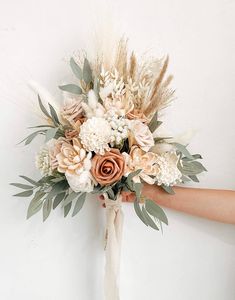 a bridal bouquet is being held by someone's hand in front of a white wall