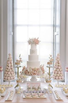 a white wedding cake with pink flowers and macaroons on the table next to it