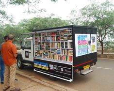 two men standing next to a truck with a book stand on the back of it