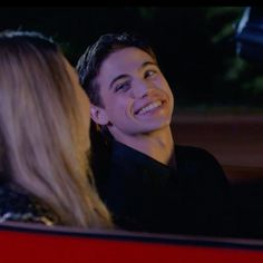 a young man and woman sitting in a car smiling at each other's eyes