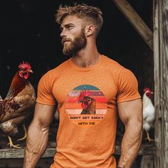 a man wearing an orange t - shirt with a rooster on it and the words don't get cocky with me