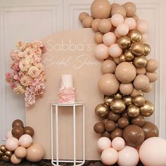 a table topped with balloons next to a cake and vase filled with pink flowers on top of it