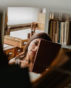 a woman reading a book in front of a bookshelf