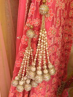 a red dress with gold and white beads hanging from it's side, in front of a curtain