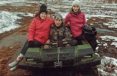 three people are sitting on an atv in the mud