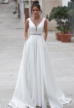 a woman in a white dress is standing on the street with her hands behind her back