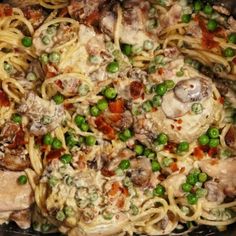 a pan filled with pasta and meat covered in sauce, peas and seasoning on the side