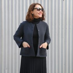 a woman standing in front of a metal wall wearing a black dress and jacket with her hands on her hips