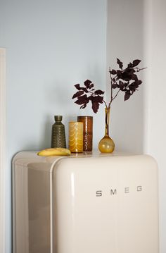 a white shelf with some vases and plants on it's side next to a clock