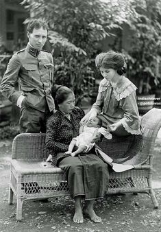 an old black and white photo of three people sitting on a bench with a baby