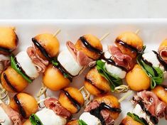 small appetizers on skewers with meat, cheese and sauce are arranged on a white platter