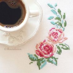 a cup of coffee sitting on top of a table next to a cross stitch pattern