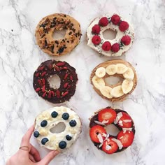 six donuts with different toppings on them sitting on a marble counter top next to a person's hand