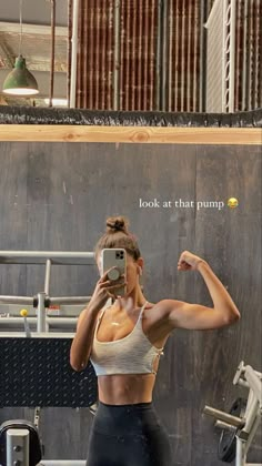 a woman taking a selfie with her cell phone in front of a gym machine