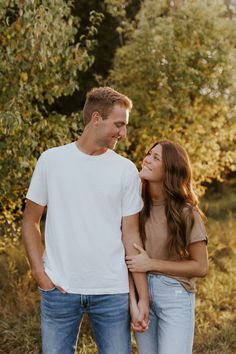 a young man and woman standing together in the woods looking at each other with smiles on their faces