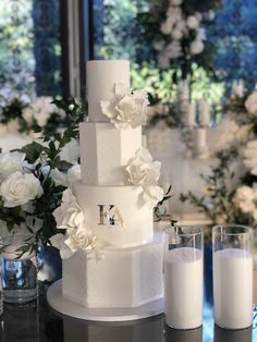 a three tiered cake with flowers on the side and two glasses next to it