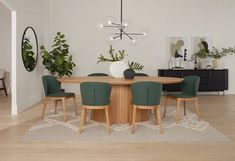 a dining room table surrounded by green chairs and potted plants on top of a rug