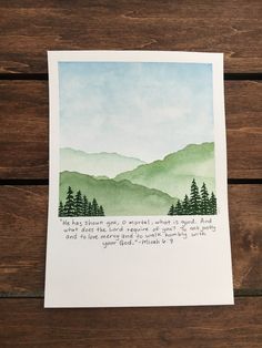 a card with an illustration of mountains and trees in the background, on top of a wooden table