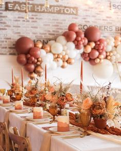 a long table with candles and flowers in front of a brick wall decorated with balloons