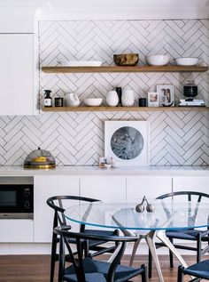 the kitchen shelves are covered in white herringbone tiles and glass top dining room table