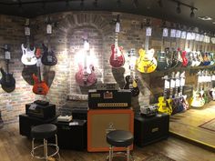 guitars and amps are on display in a music store with brick walls, wooden floors and stools