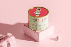 a can of rocketo sitting on top of a pink surface next to a white object