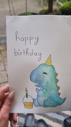 a person holding up a birthday card with a dinosaur on it