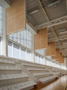 rows of empty white seats in a large room with wood flooring and high windows