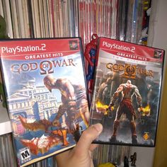 two video games being held up in front of a shelf