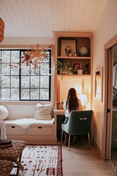 a woman sitting on a chair in front of a window next to a rug and lamp