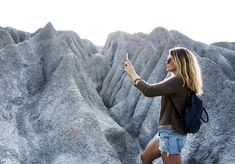 a woman taking a selfie with her cell phone in front of some mountains and rocks